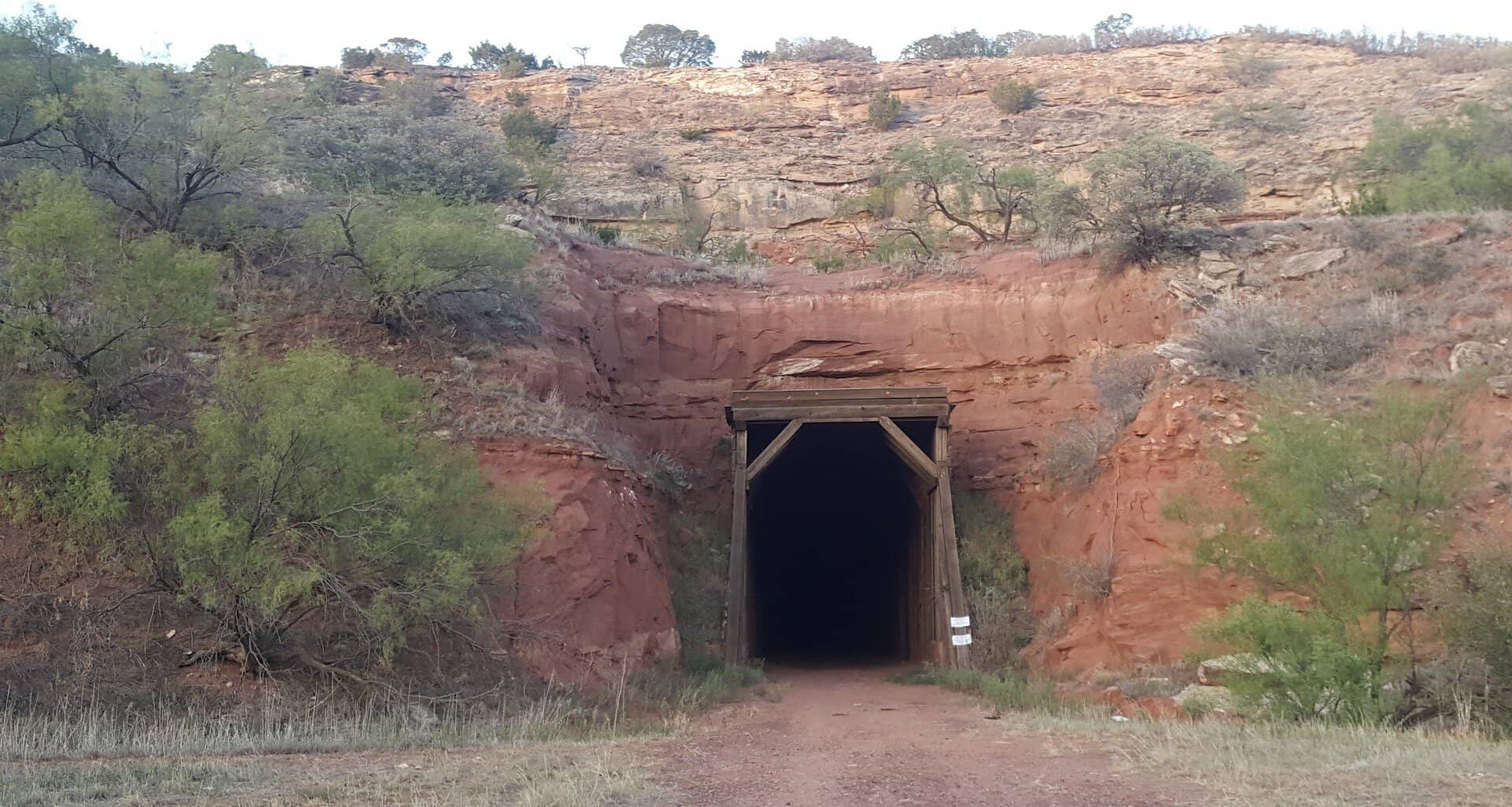 The dark Clarity Tunnel portal cut into the red rock ridge on the Caprock Canyons Trailway near Quitaque, Texas