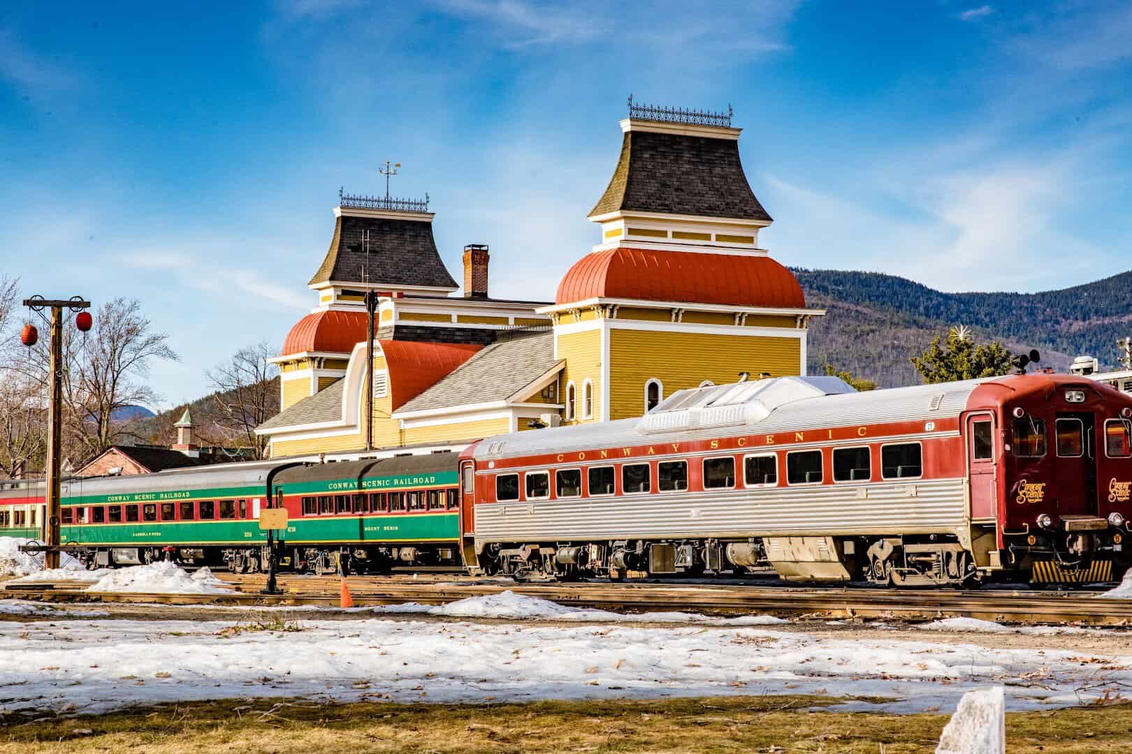 The ornate Victorian Conway Scenic Railroad depot with vintage rail cars and snow on the ground in North Conway, New Hampshire