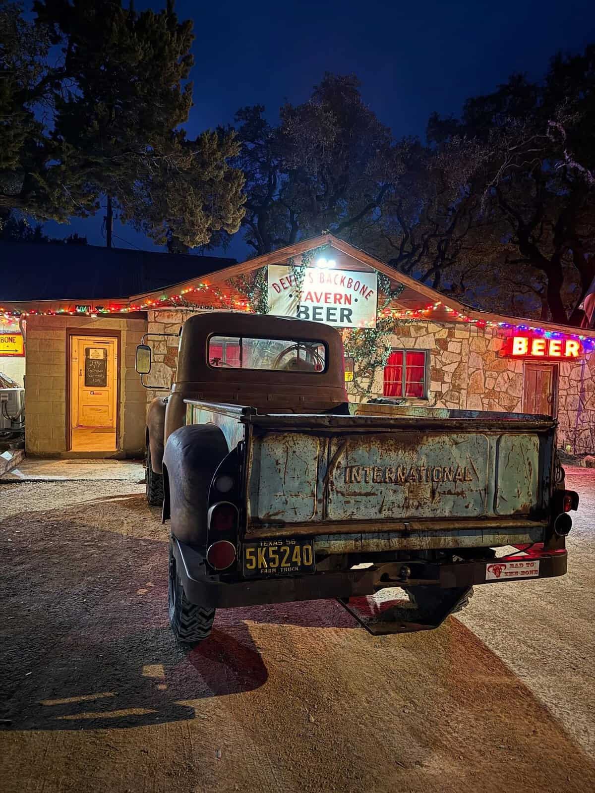 Devil's Backbone Tavern lit up at night with a vintage truck out front in Fischer, Texas