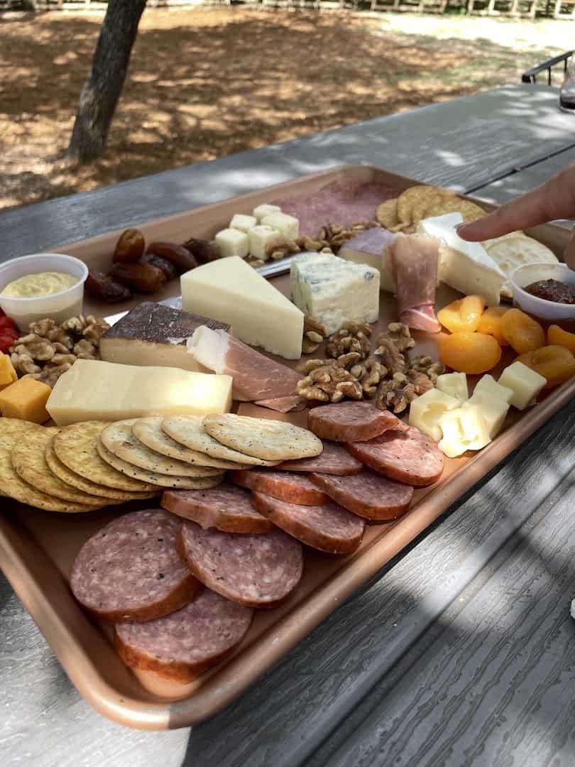 A loaded charcuterie board with meats and cheeses on a picnic table in Driftwood, Texas