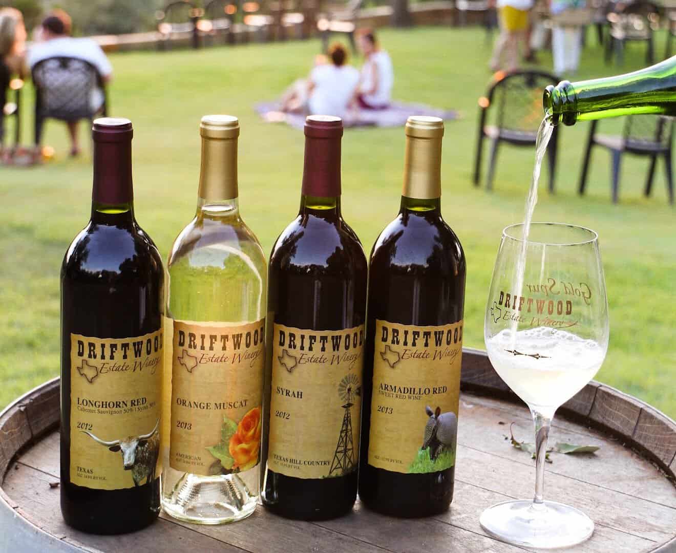 A lineup of Driftwood Estate wine bottles and a glass on a barrel