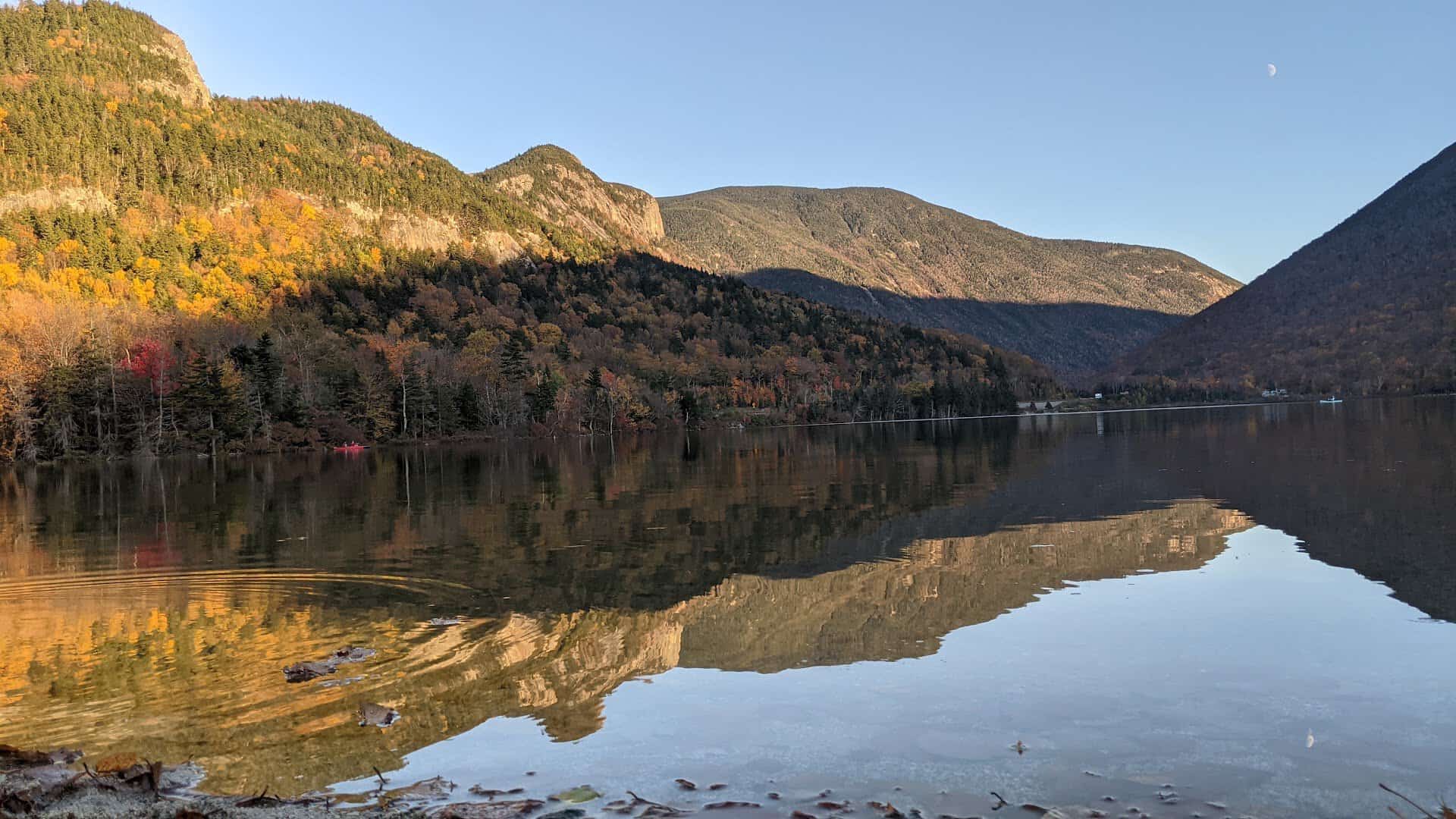 Cliffs and ridgeline of Franconia Notch mirrored in the glassy water of Echo Lake, New Hampshire, in full autumn color