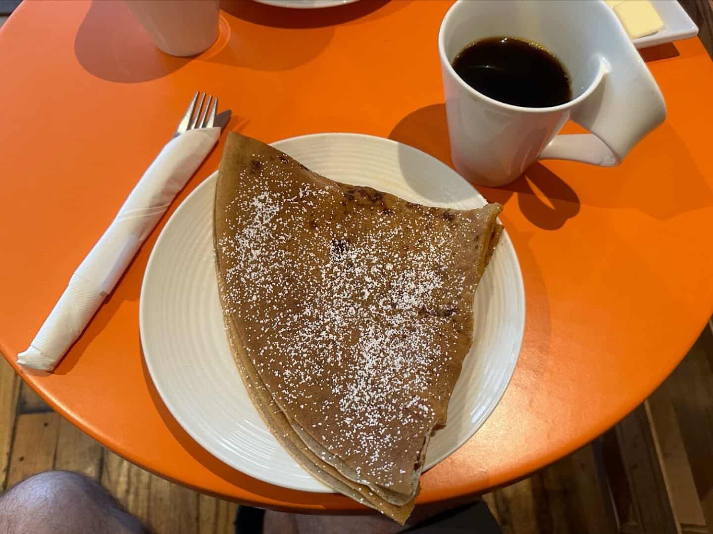 French crepe on an orange plate with a cup of coffee at La Boulangerie in San Antonio