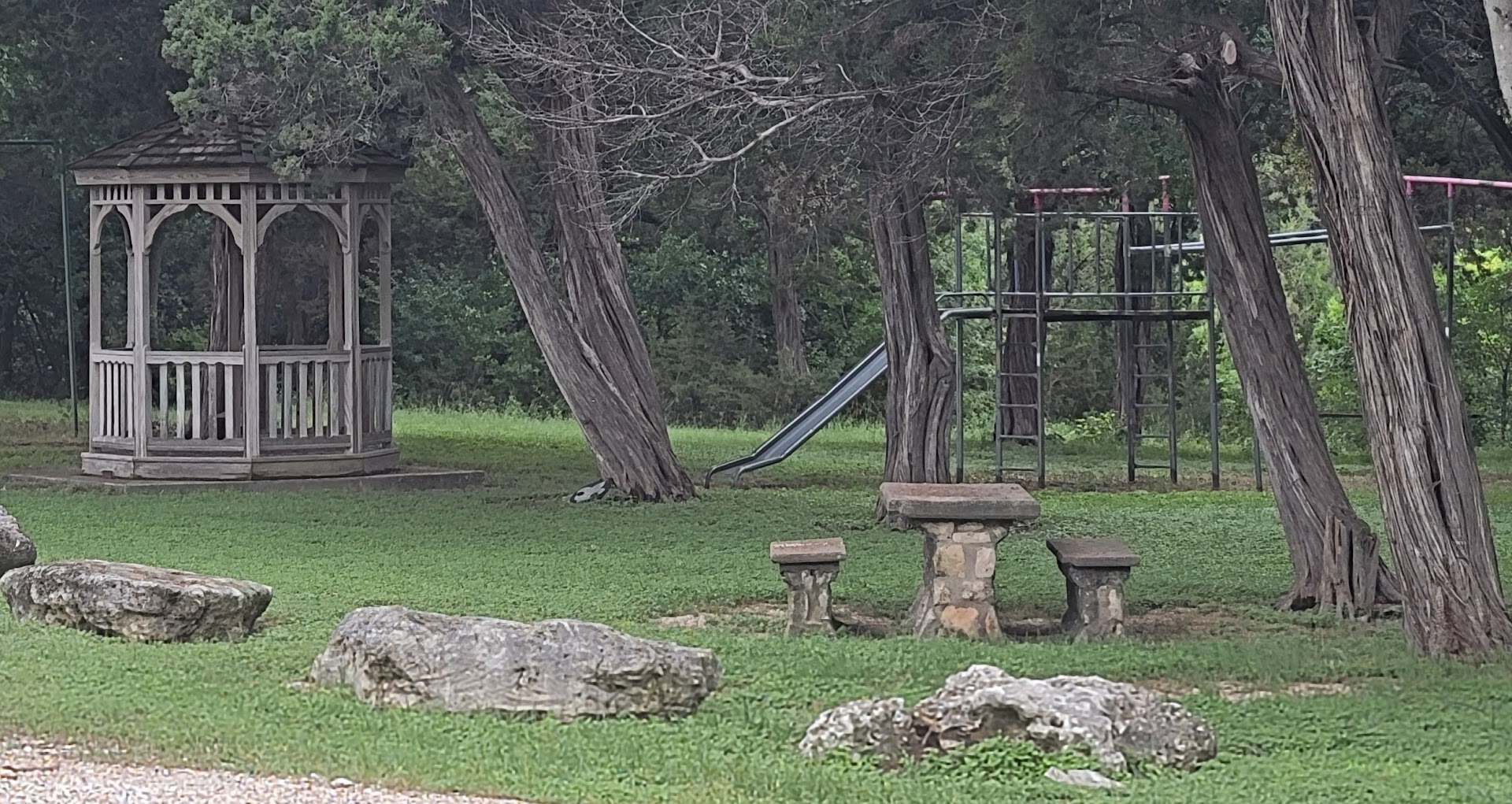 Gazebo, stone picnic tables and playground under the trees at Tonkawa Falls City Park in Crawford, Texas