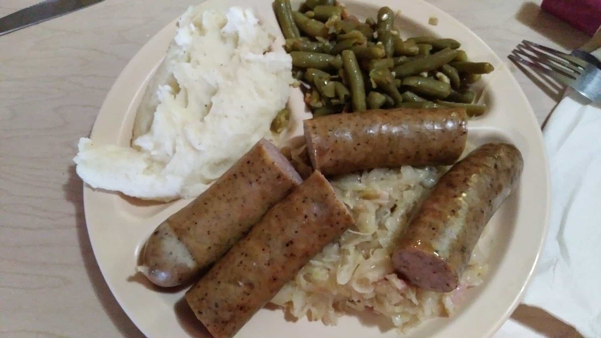 A plate of Green's smoked sausage links with sauerkraut, mashed potatoes, and green beans