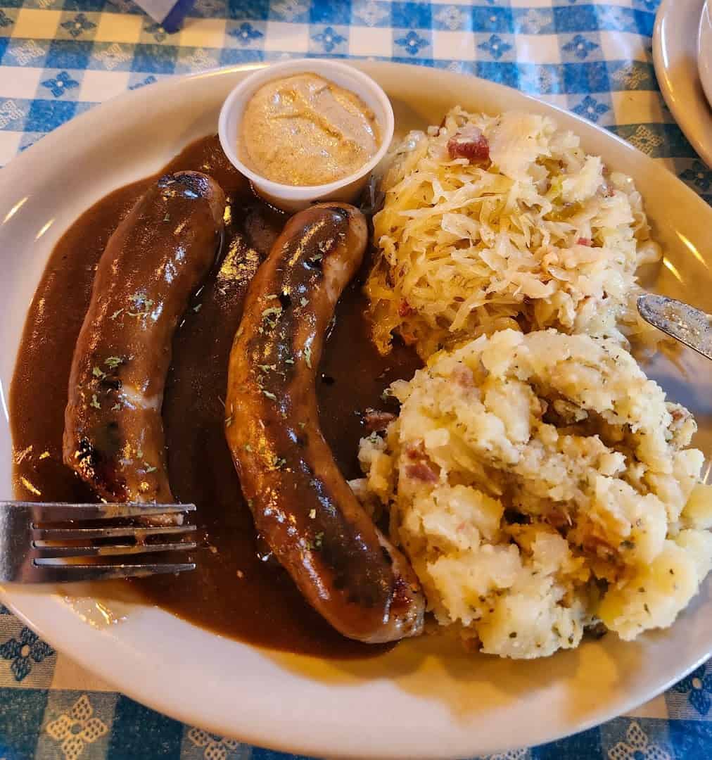 Grilled bratwurst in dark beer gravy with sauerkraut and German potato salad at Walburg German Restaurant