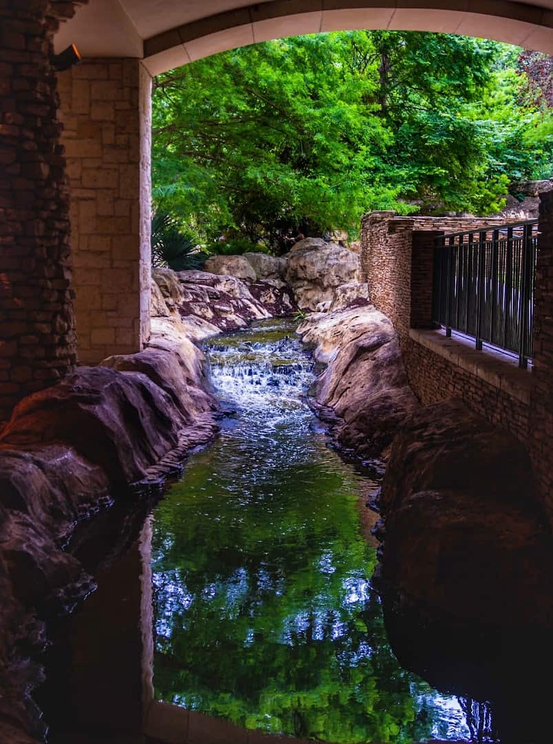 Waterfall flowing through a stone archway at The Grotto on the San Antonio River Walk