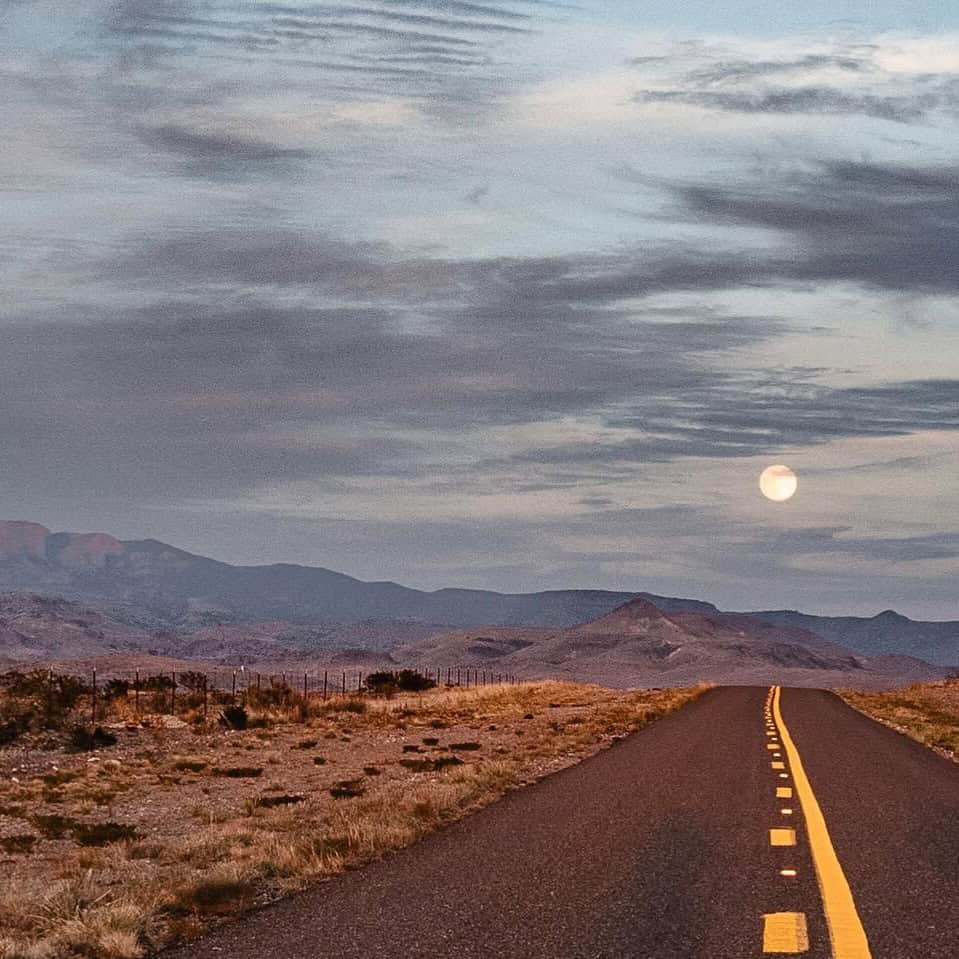 Open highway leading toward the Davis Mountains at dusk with the moon rising, West Texas