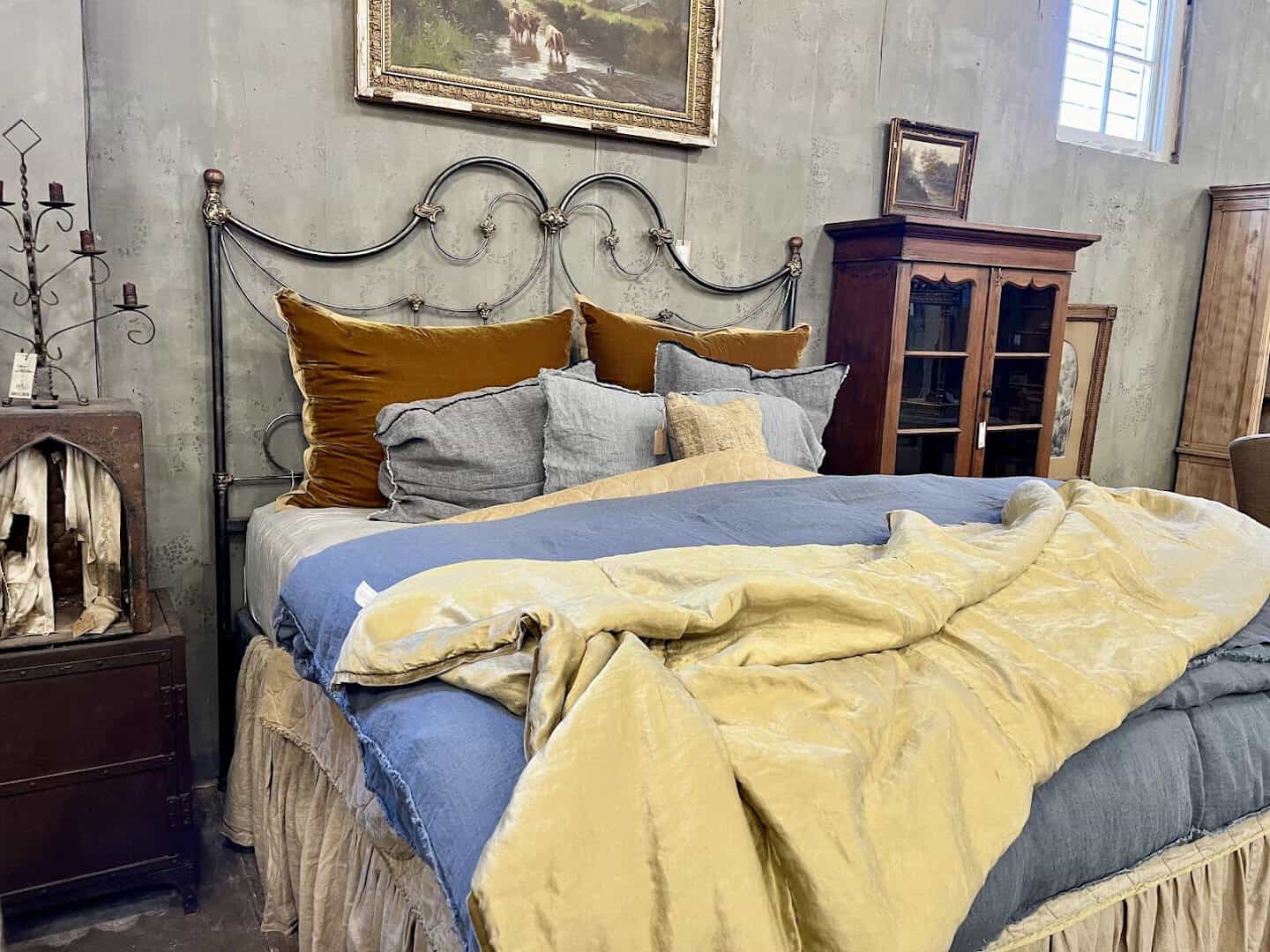 Antique iron bed dressed in velvet and linen bedding at Carol Hicks Bolton Antiques in Fredericksburg
