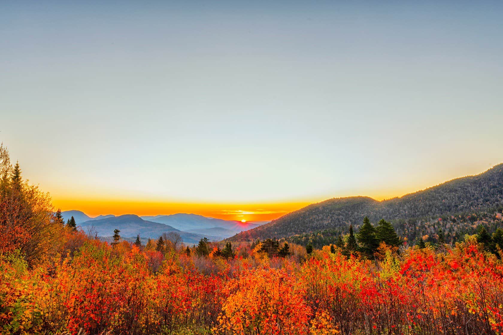 Sunrise over red and orange fall foliage along the Kancamagus Highway in Lincoln, New Hampshire