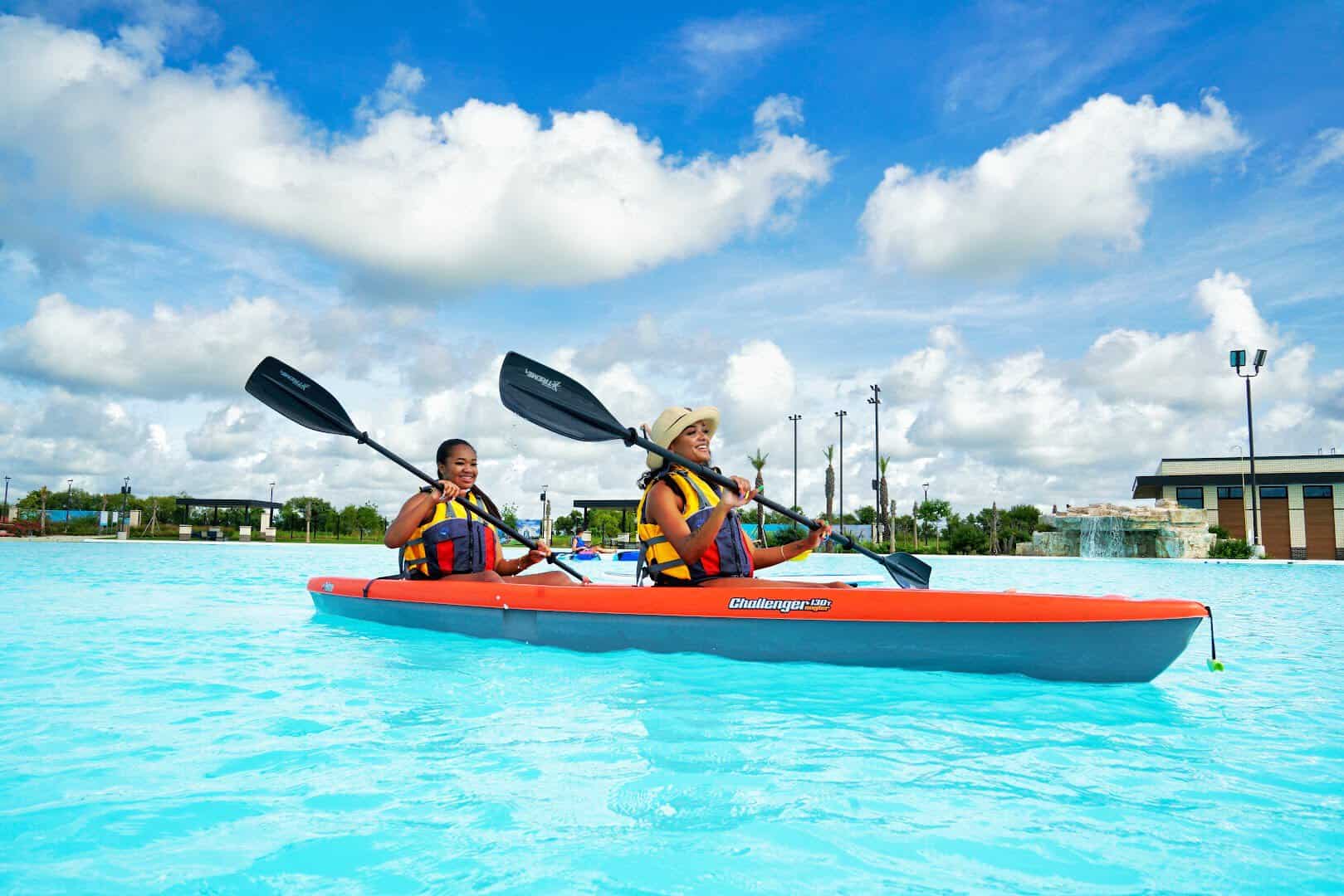 Two kayakers paddling across the clear turquoise Crystal Lagoon at Lago Mar in Texas City