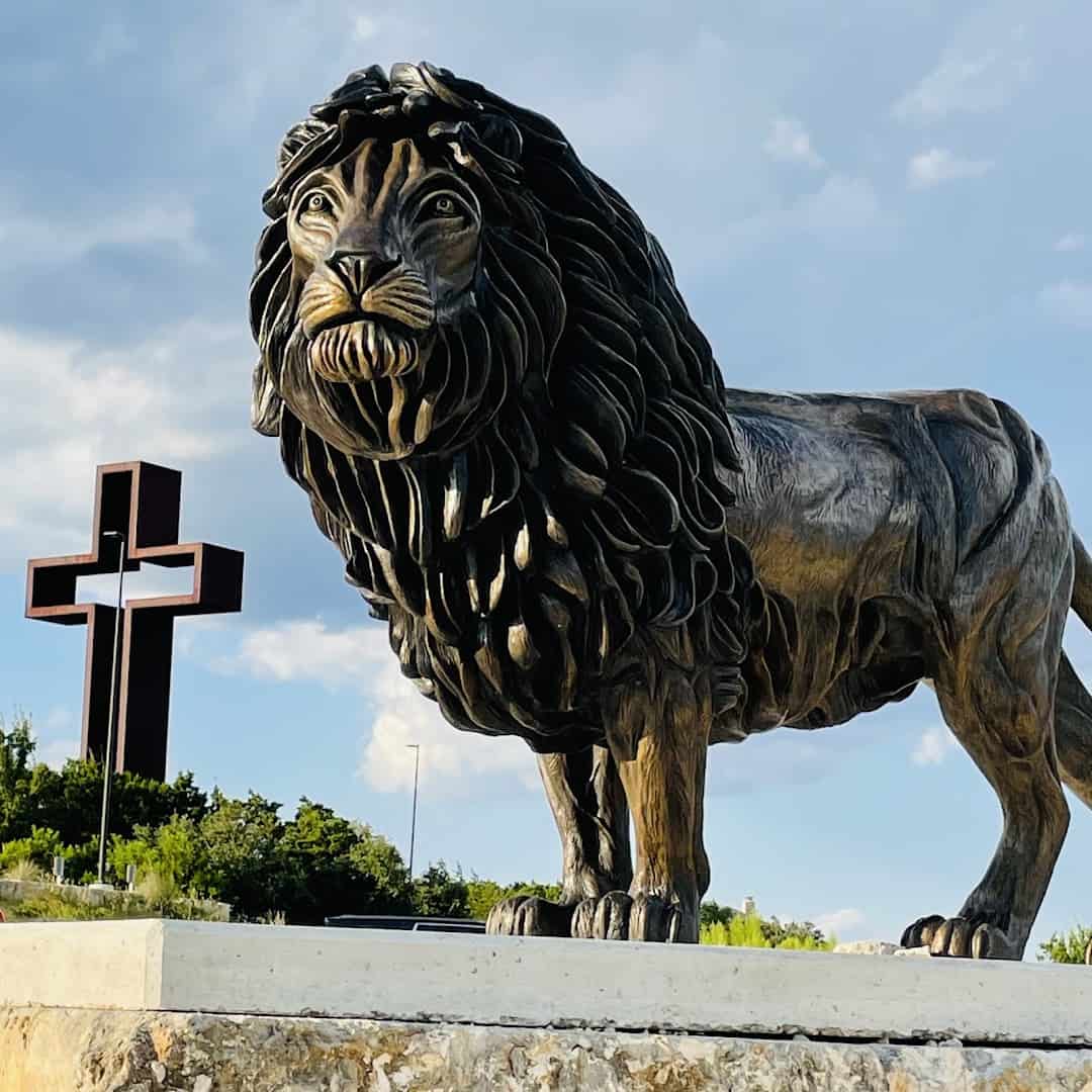Lion of Judah bronze sculpture with the Empty Cross behind it at the Coming King Sculpture Prayer Garden