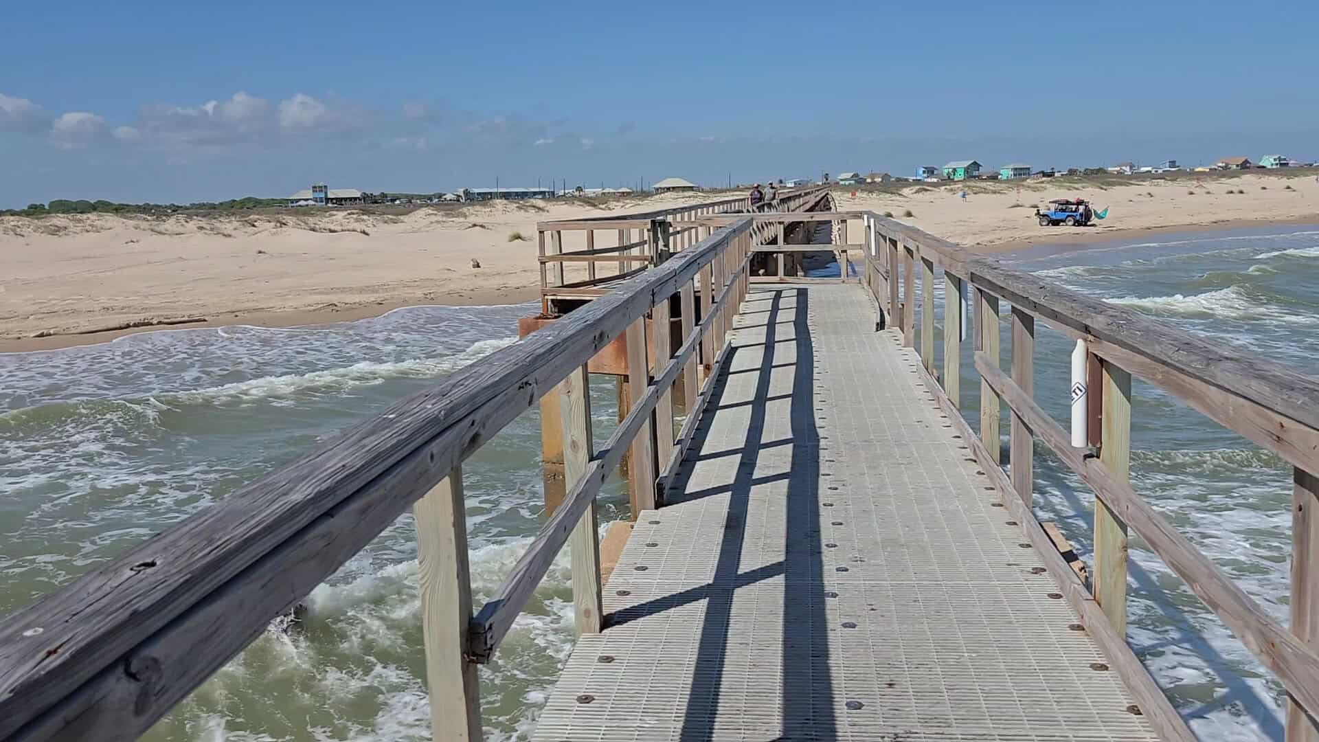 Wooden pier stretching over the surf toward the beach at Matagorda Bay Nature Park in Matagorda, Texas