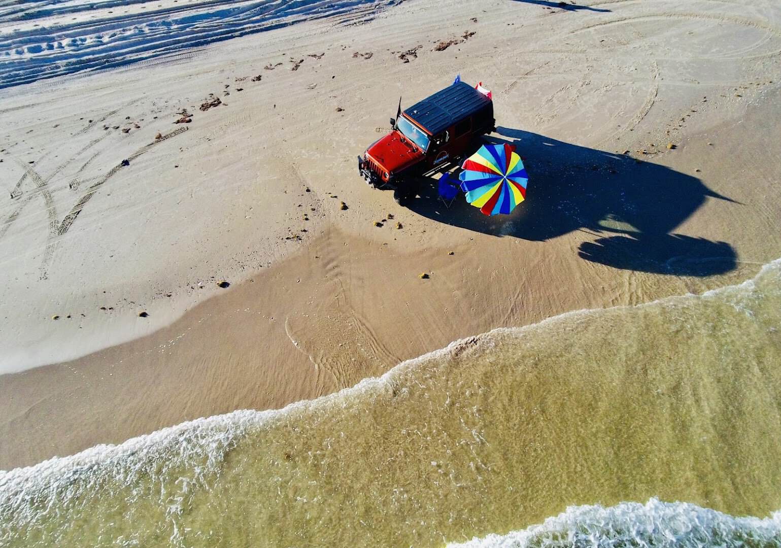 A vehicle and beach umbrella parked on the firm sand at the waterline of Matagorda Beach, Texas