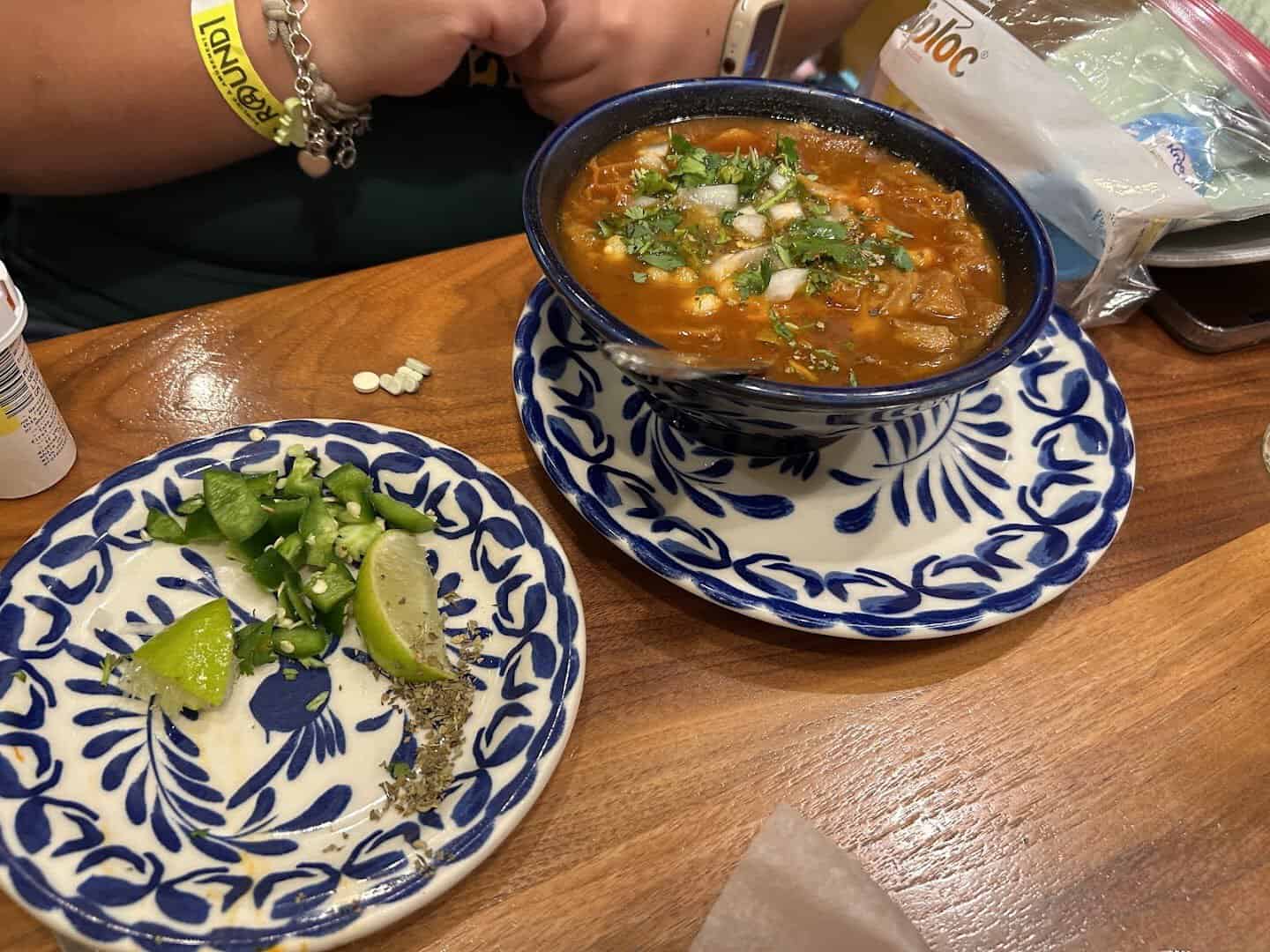 Bowl of red-broth menudo with onion and cilantro at Mi Familia at the Rim in San Antonio