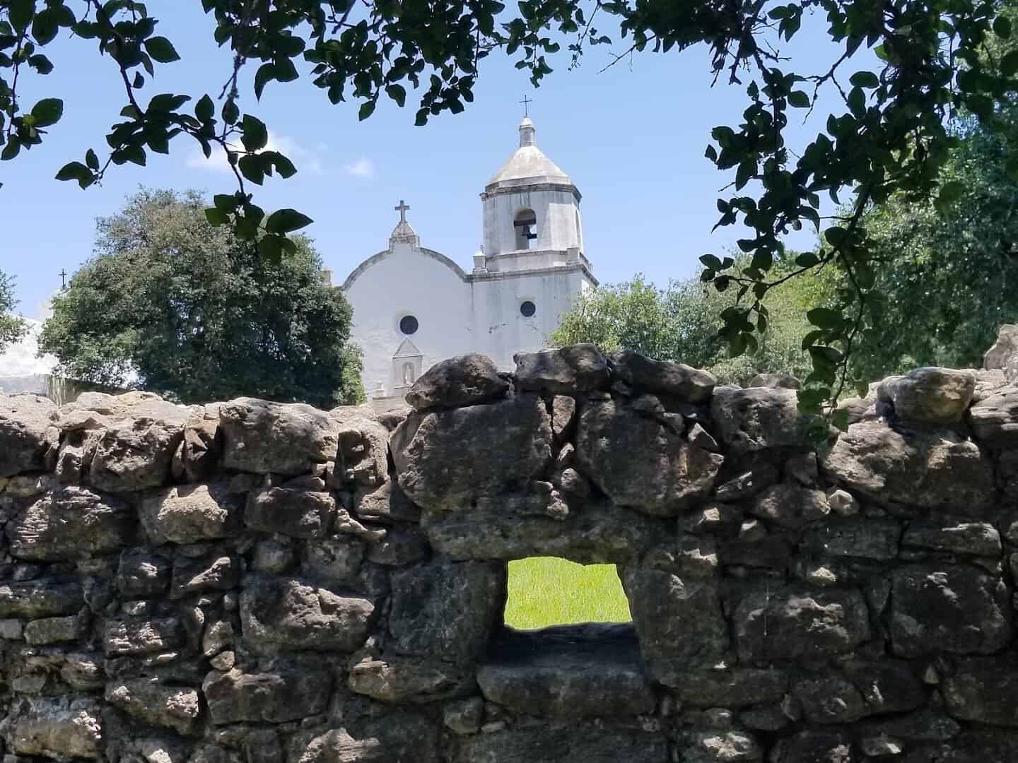 Whitewashed church of Mission Espiritu Santo framed by trees at Goliad State Park