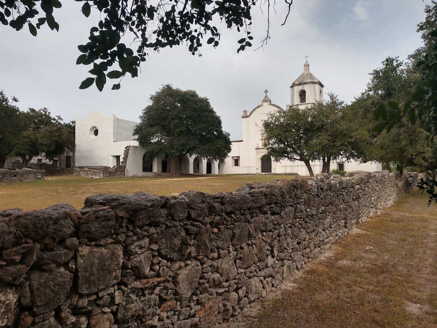 Rough stone wall in front of the whitewashed mission church at Goliad State Park