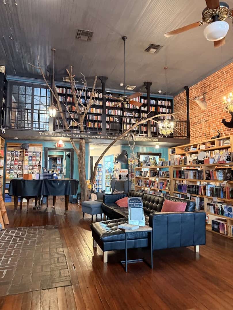 Interior of The Painted Porch Bookshop in Bastrop, Texas, with a tree, book-lined mezzanine and leather lounge chairs
