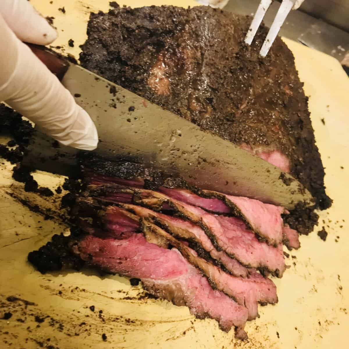 Slicing house-cured pastrami showing its peppery crust at Kenny & Ziggy's in Houston