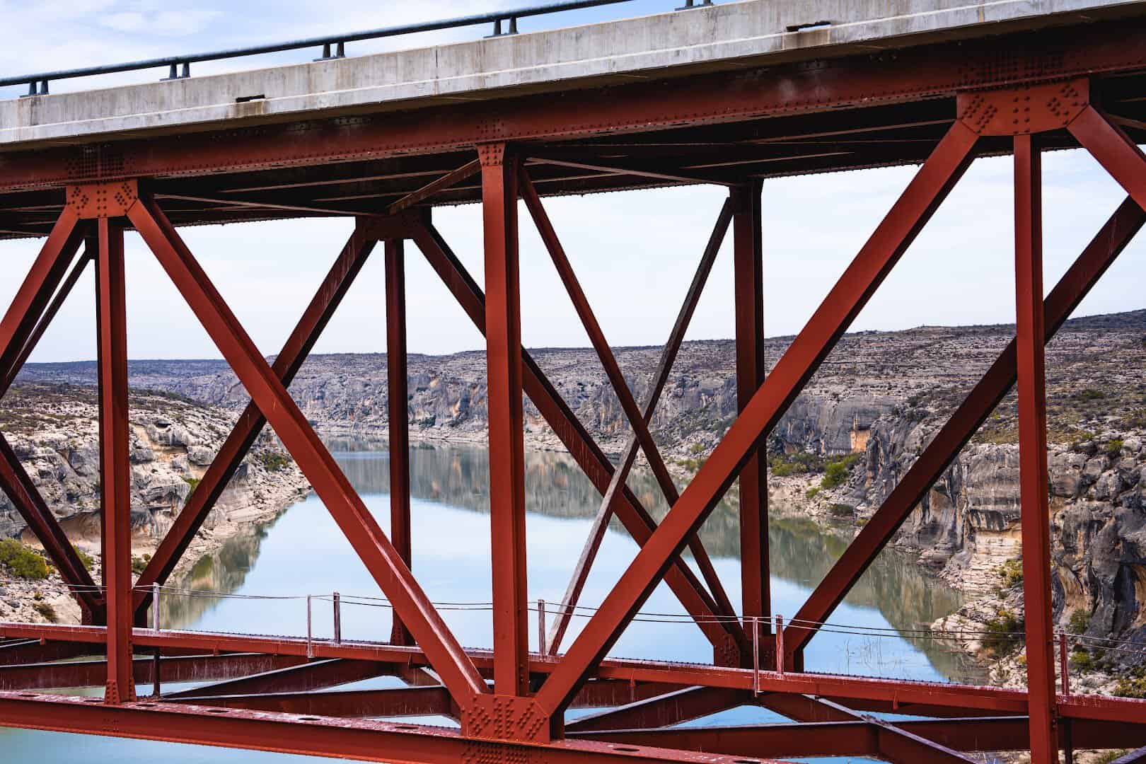 Red steel deck truss of the Pecos River High Bridge with the river far below