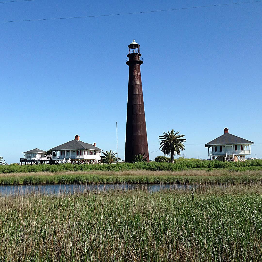 The cast iron Point Bolivar Lighthouse rising above stilted homes in Port Bolivar Texas