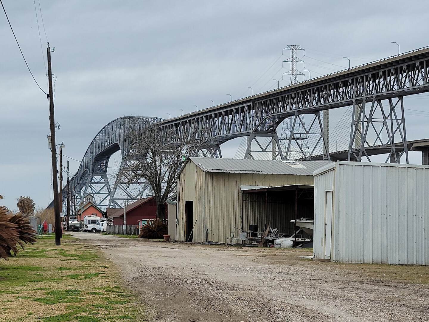 The steel arch of the Rainbow Bridge towering over waterfront boat sheds near Bridge City, Texas