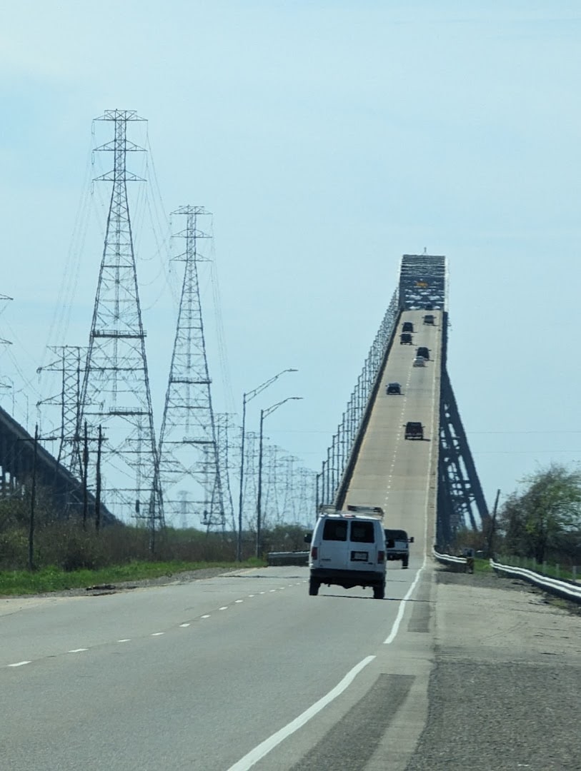 Driving up the steep climb of the Rainbow Bridge deck toward open sky near Port Arthur, Texas
