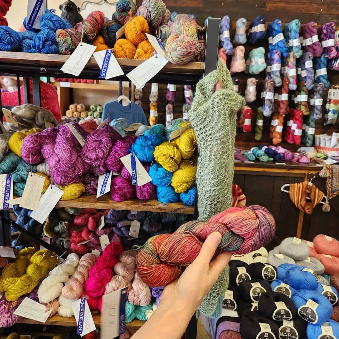 A hand reaching for a skein on a shelf of colorful yarn at Lone Star Yarn in Bedford, Texas