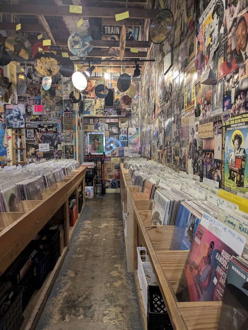 Aisle of vinyl record crates under poster covered walls at Sigs Lagoon in Houston