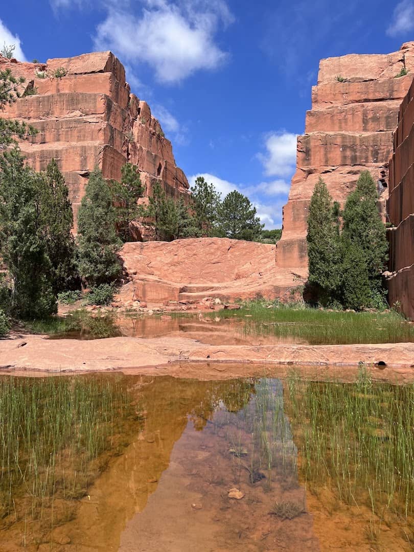 Fiery red sandstone walls reflected in water at Red Rock Canyon Open Space, Colorado Springs, Colorado