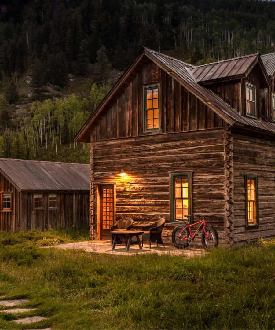 A restored hand-hewn log cabin glowing at dusk at Dunton Hot Springs, Dolores, Colorado