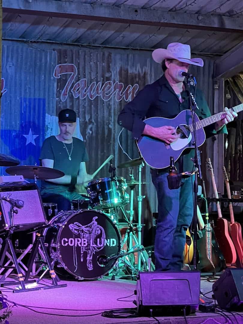 A cowboy-hatted singer performing on the stage at Riley's Tavern in Hunter, Texas