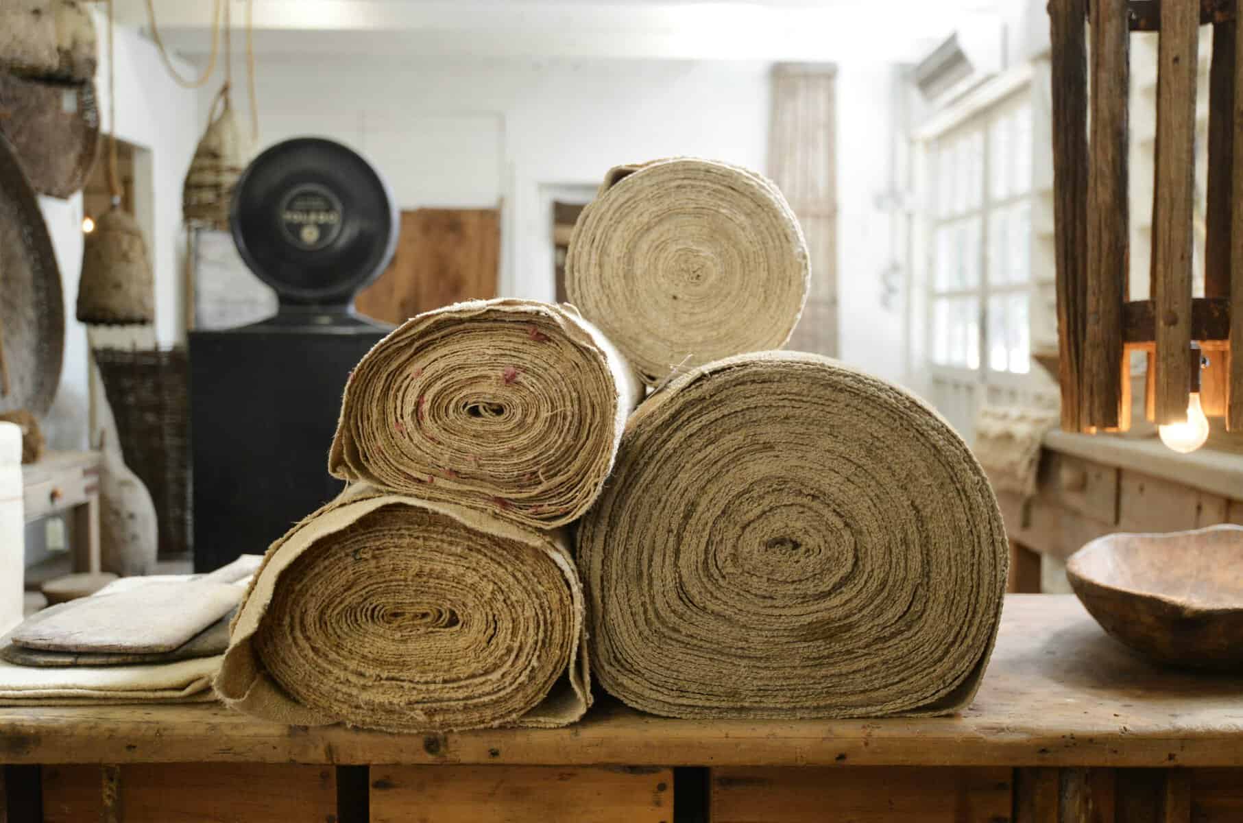 Rolls of antique European linen and hemp fabric stacked on a table at Carol Hicks Bolton Antiquites in Fredericksburg