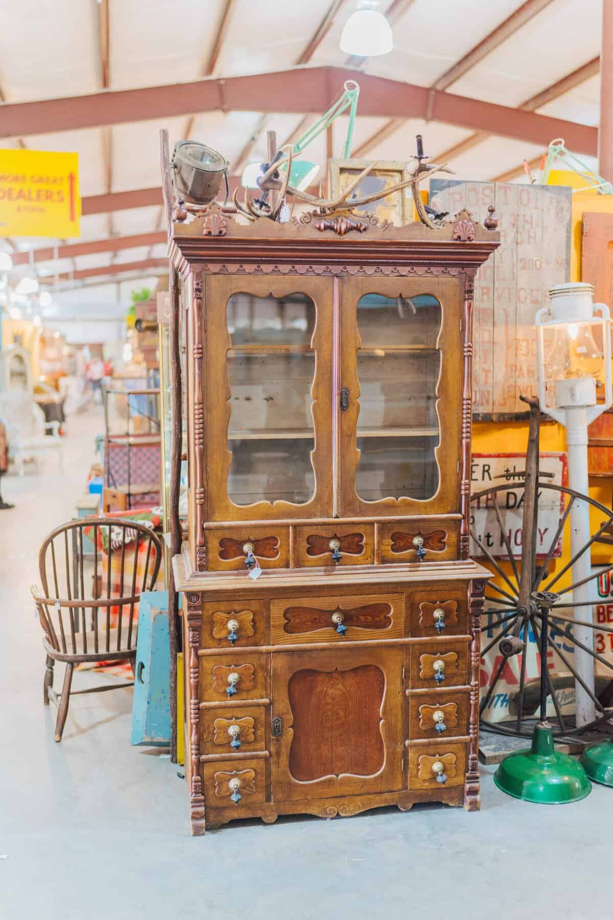Tall antique wooden china hutch with a green glass lamp at the Round Top antiques fair