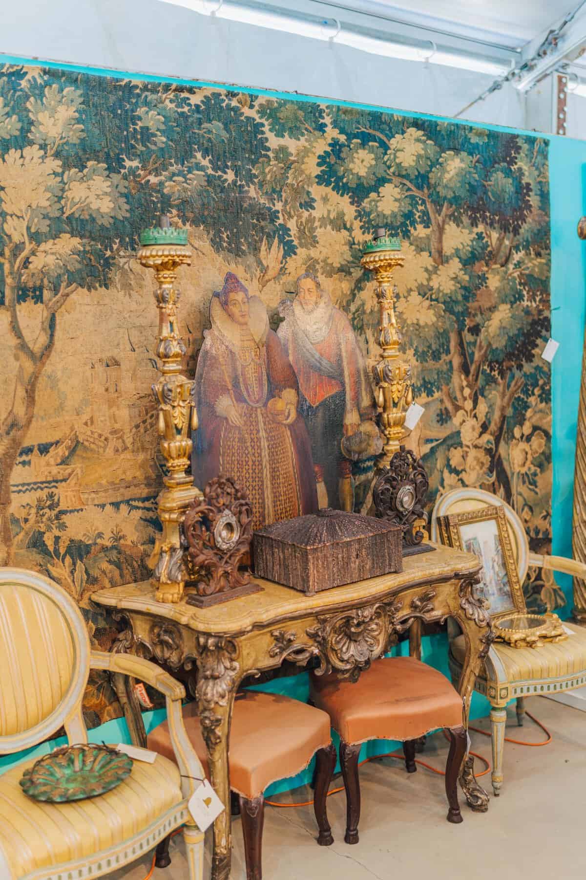 Staged antique vignette with a tapestry, carved chairs and a mirror at the Round Top antiques fair