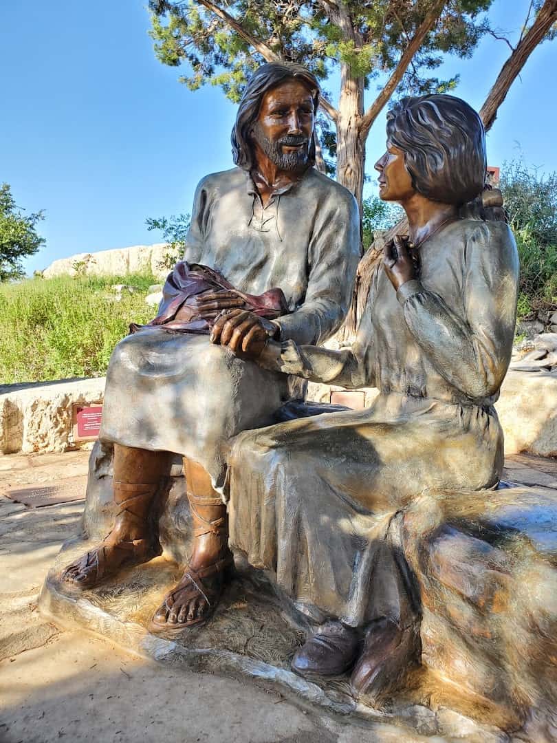 Seated bronze figures under the trees at the Coming King Sculpture Prayer Garden