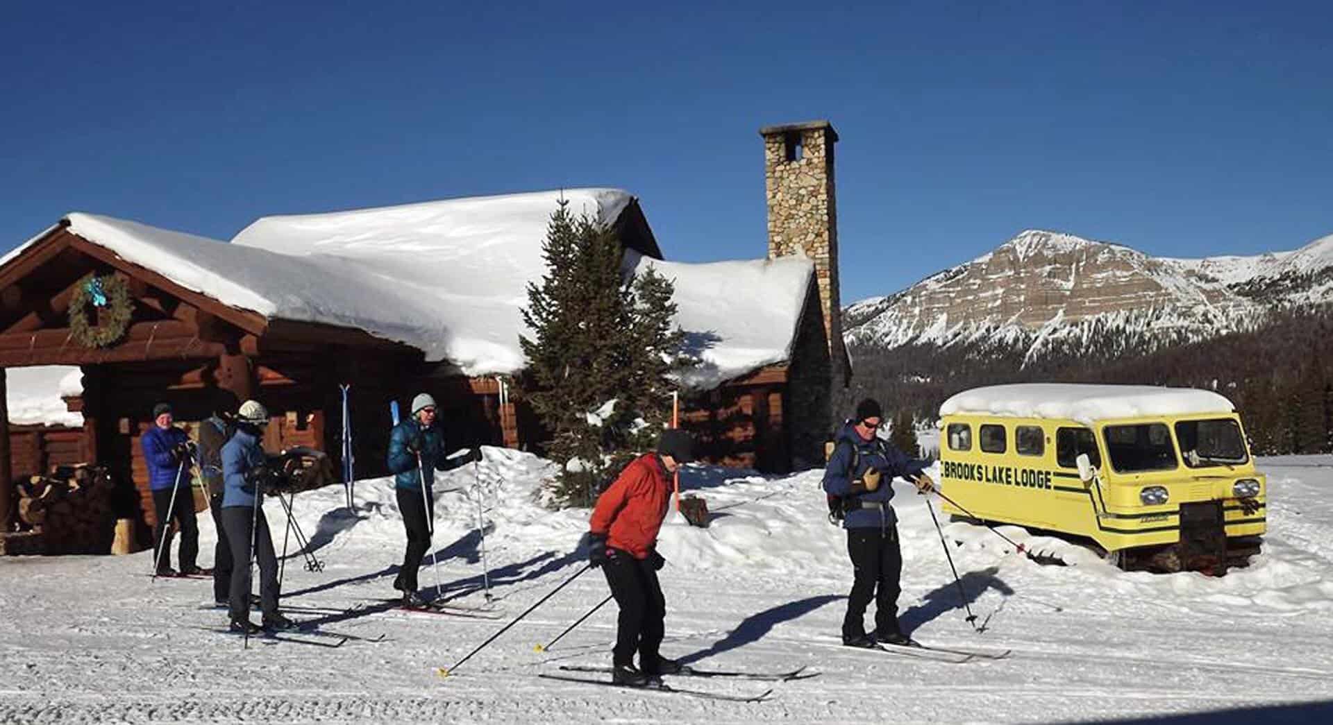 Snow-buried log lodge with cross-country skiers and a yellow snowcoach, Brooks Lake Lodge, Dubois, Wyoming