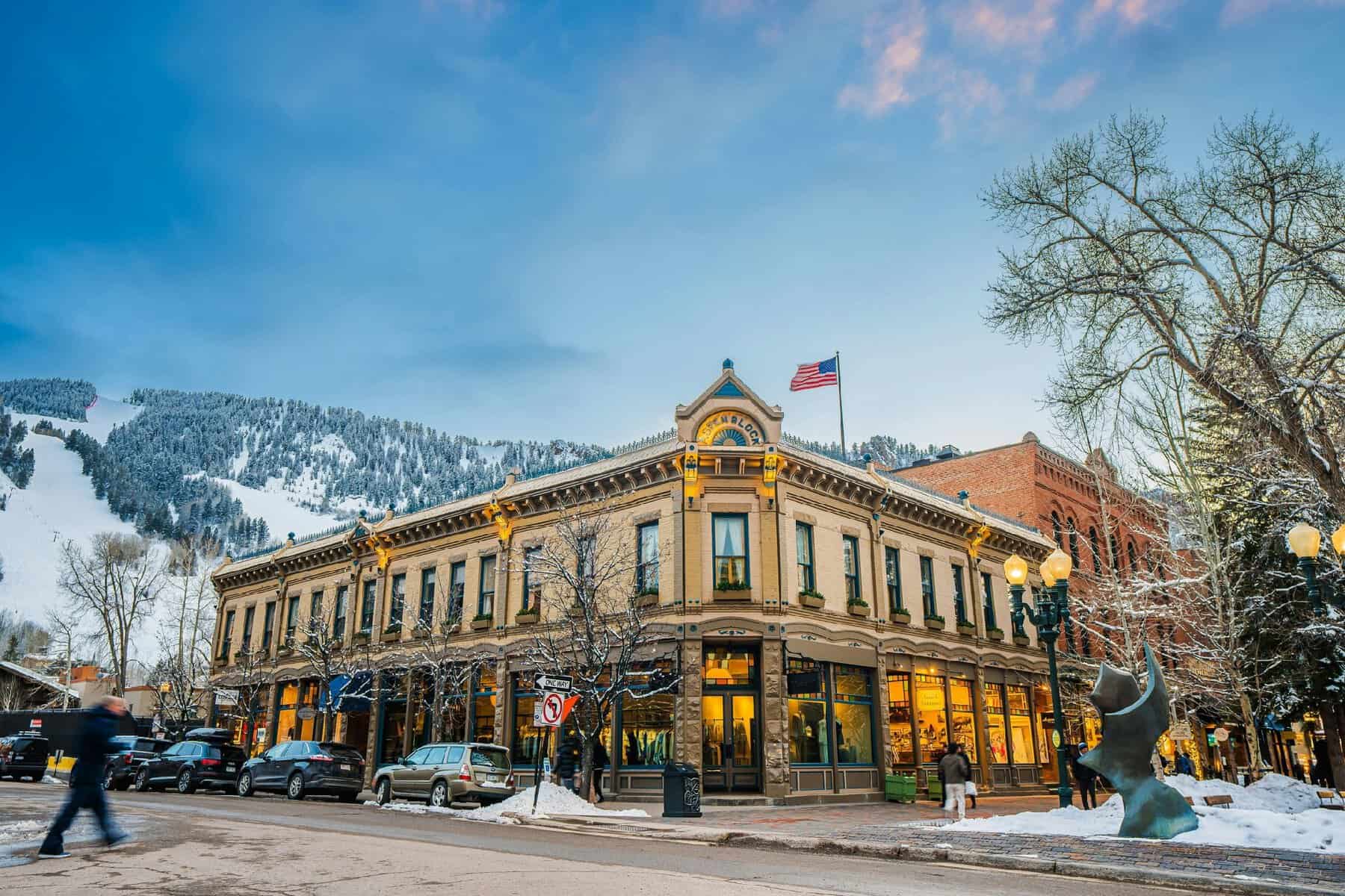 Historic Victorian storefronts and a snowy ski mountain in downtown Aspen, Colorado at dusk
