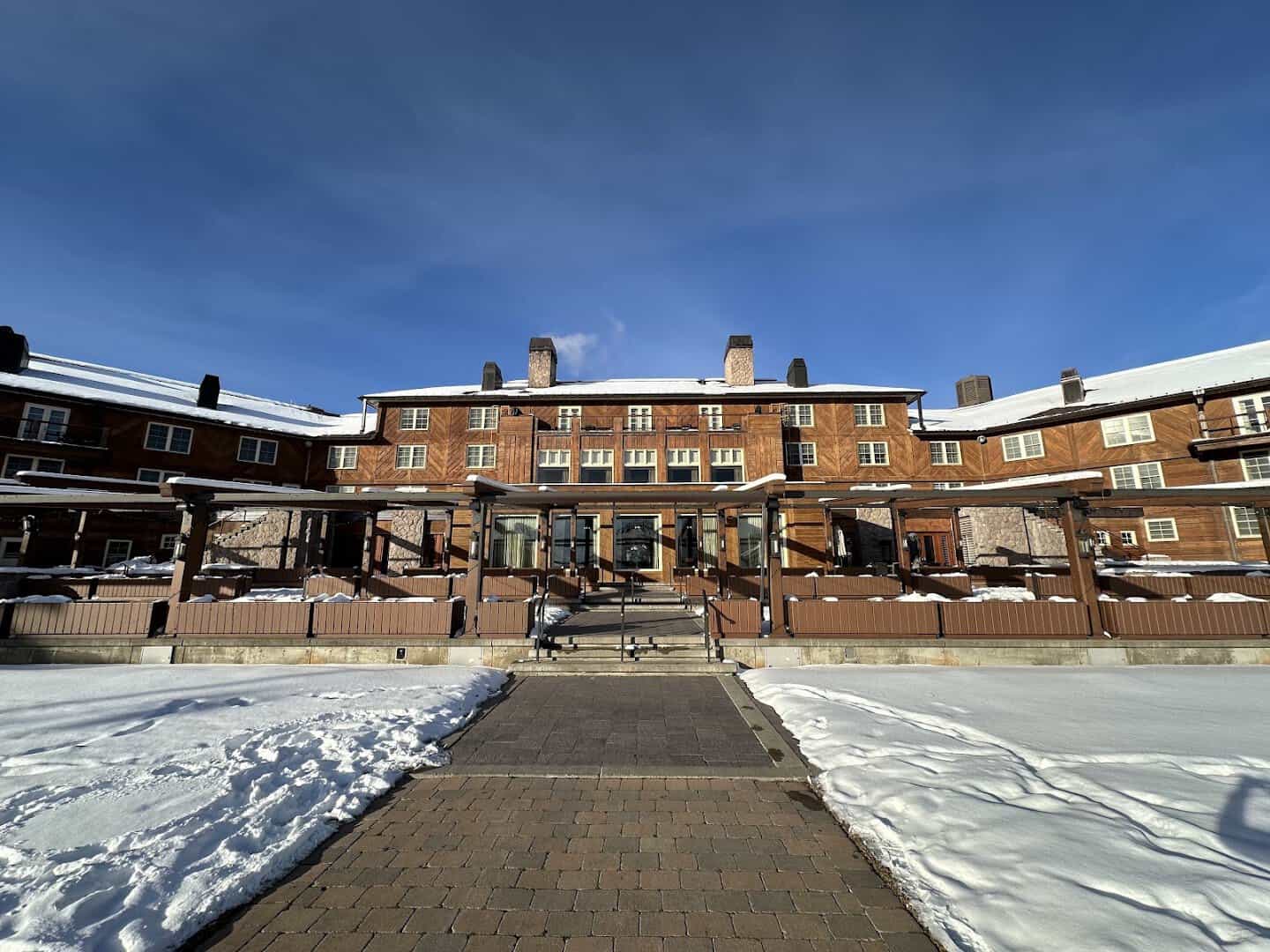 The historic timber Sun Valley Lodge behind deep snowbanks and a cleared walkway under a blue winter sky in Sun Valley, Idaho