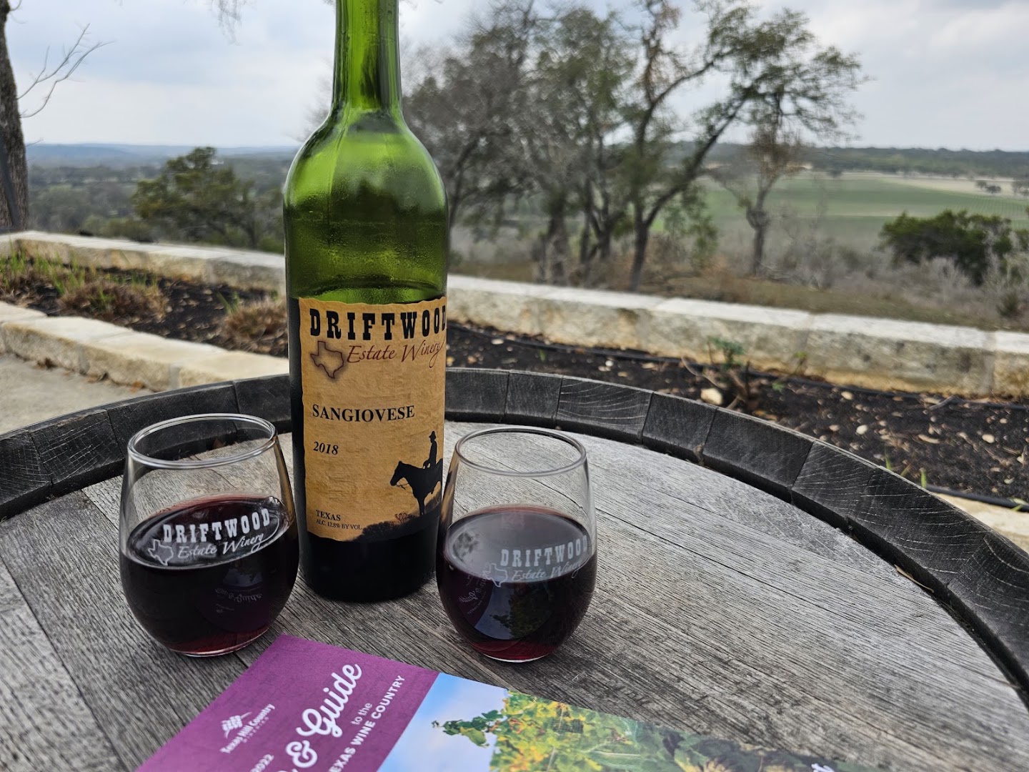 A bottle of Texas red wine and glasses with a Hill Country view near Driftwood