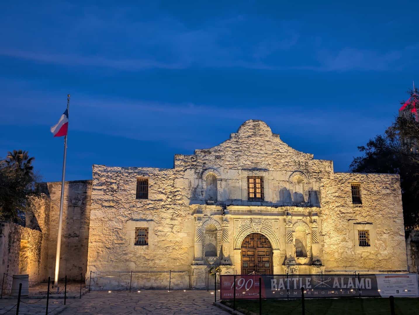 The floodlit limestone facade of the Alamo at dusk with the Texas flag, San Antonio, Texas