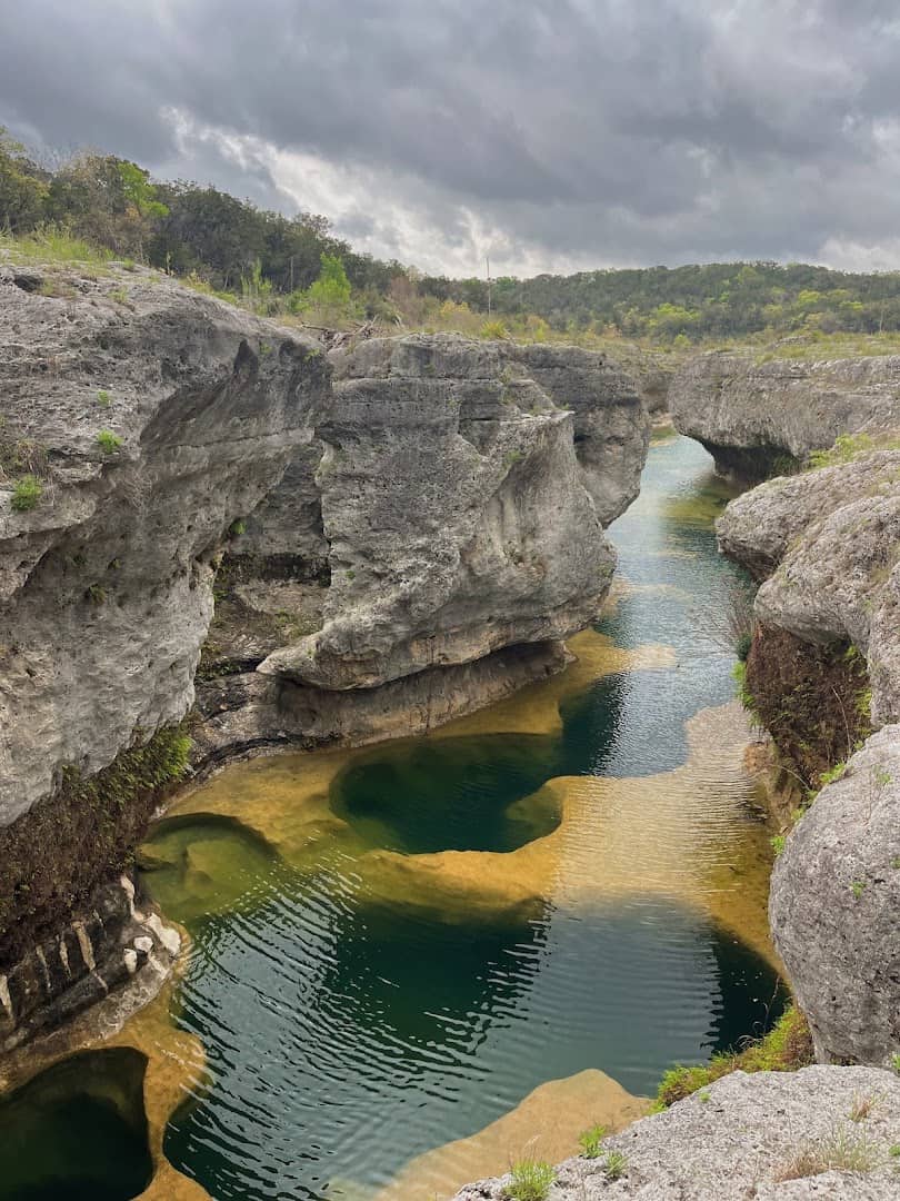 Deep green and near-black spring-fed pools between limestone walls at The Narrows on the Blanco River, Texas