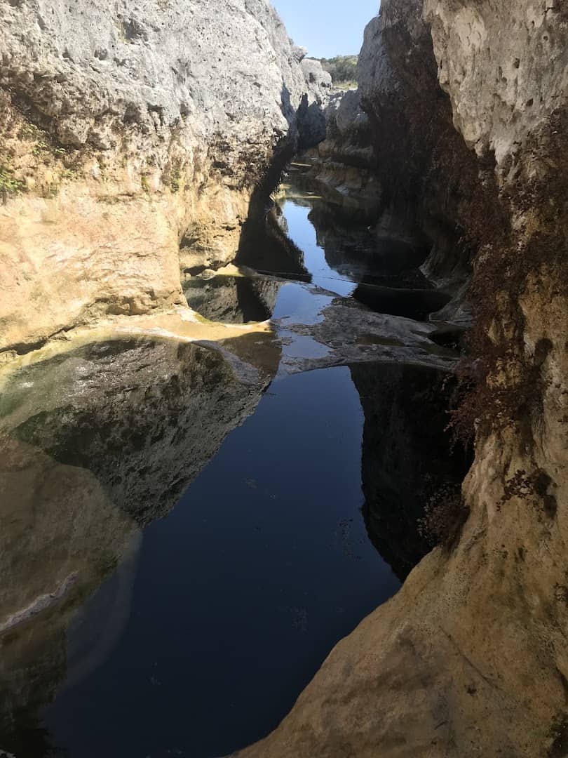 A deep, still pool reflecting the limestone gorge at The Narrows on the Blanco River, Texas