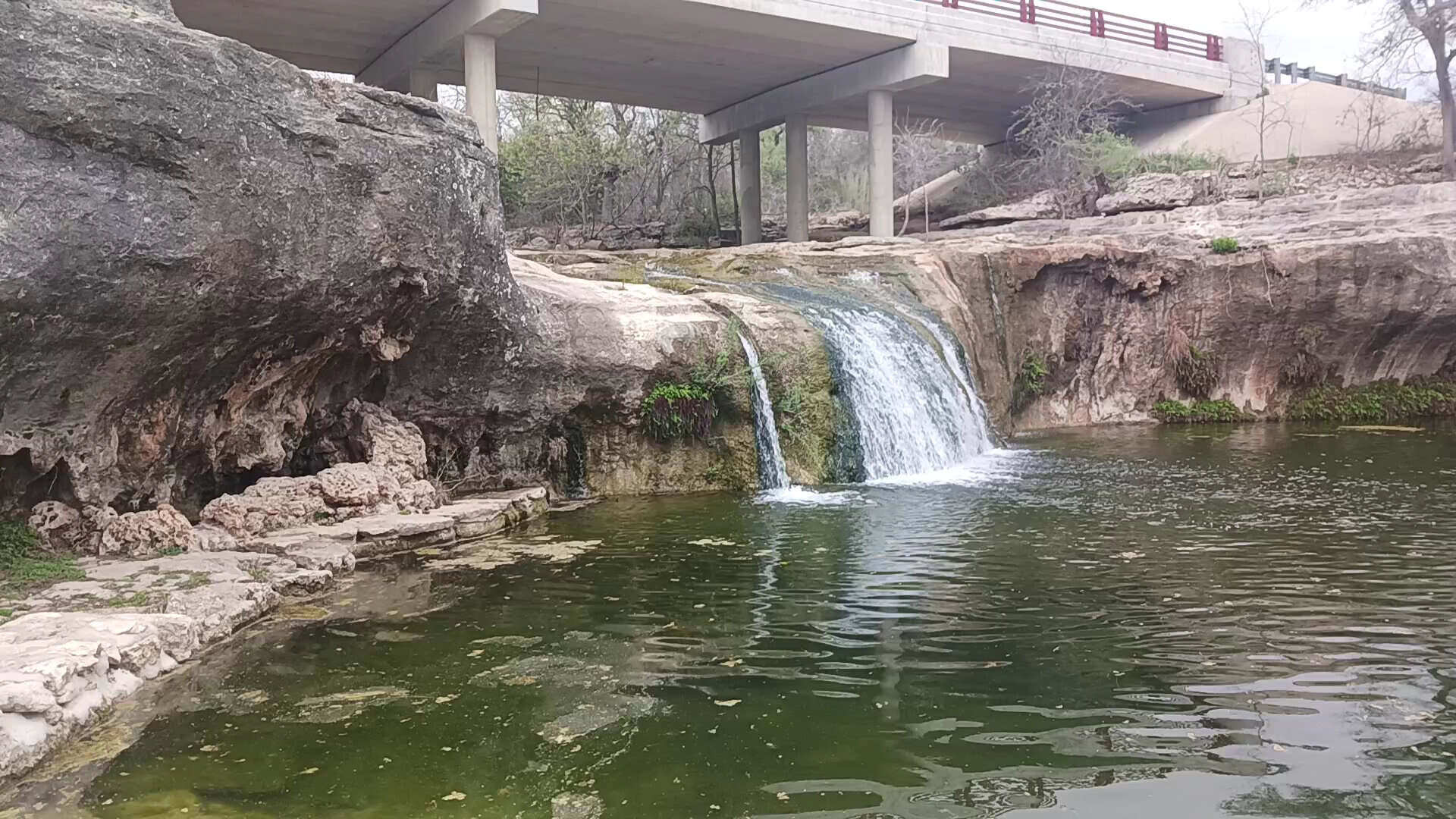 Tonkawa Falls flowing beneath the road bridge into the creek pool in Crawford, Texas