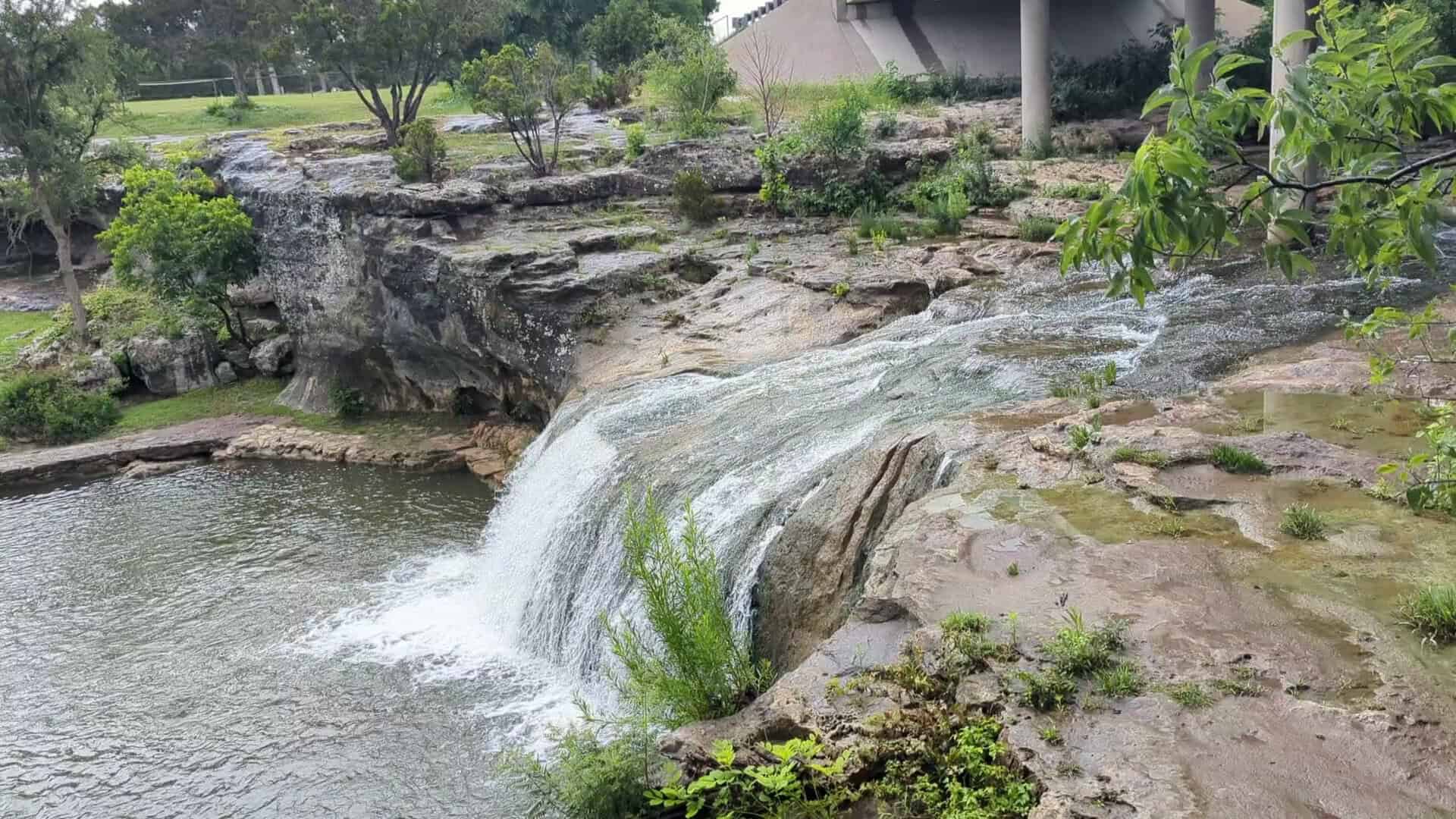 Tonkawa Falls cascading wide over the rock shelf into the swimming hole in Crawford, Texas