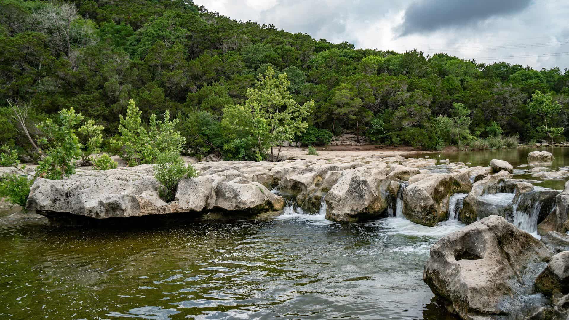 Twin streams of water spilling over limestone ledges at Twin Falls in the Barton Creek Greenbelt, Austin
