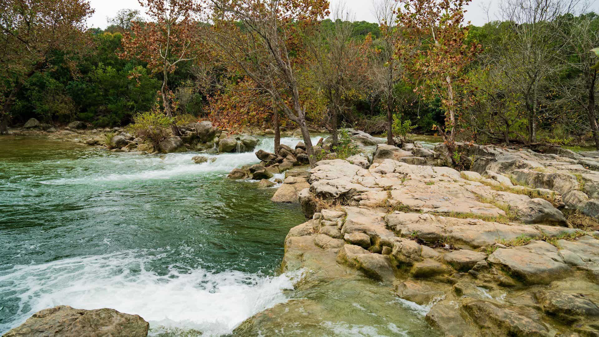 Waterfall pouring over limestone ledges into a green pool at Twin Falls in the Barton Creek Greenbelt, Austin