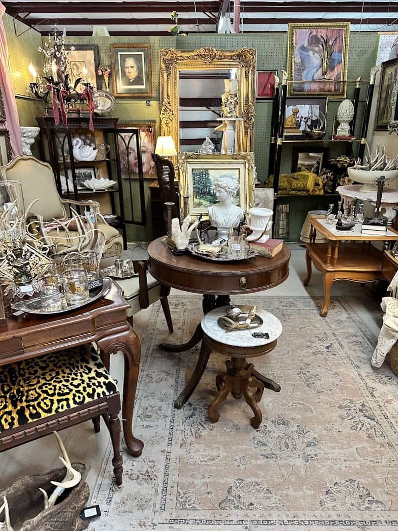 Vendor booth with a gilt mirror, round table and framed art at The Antique Gallery of Houston in Spring Texas