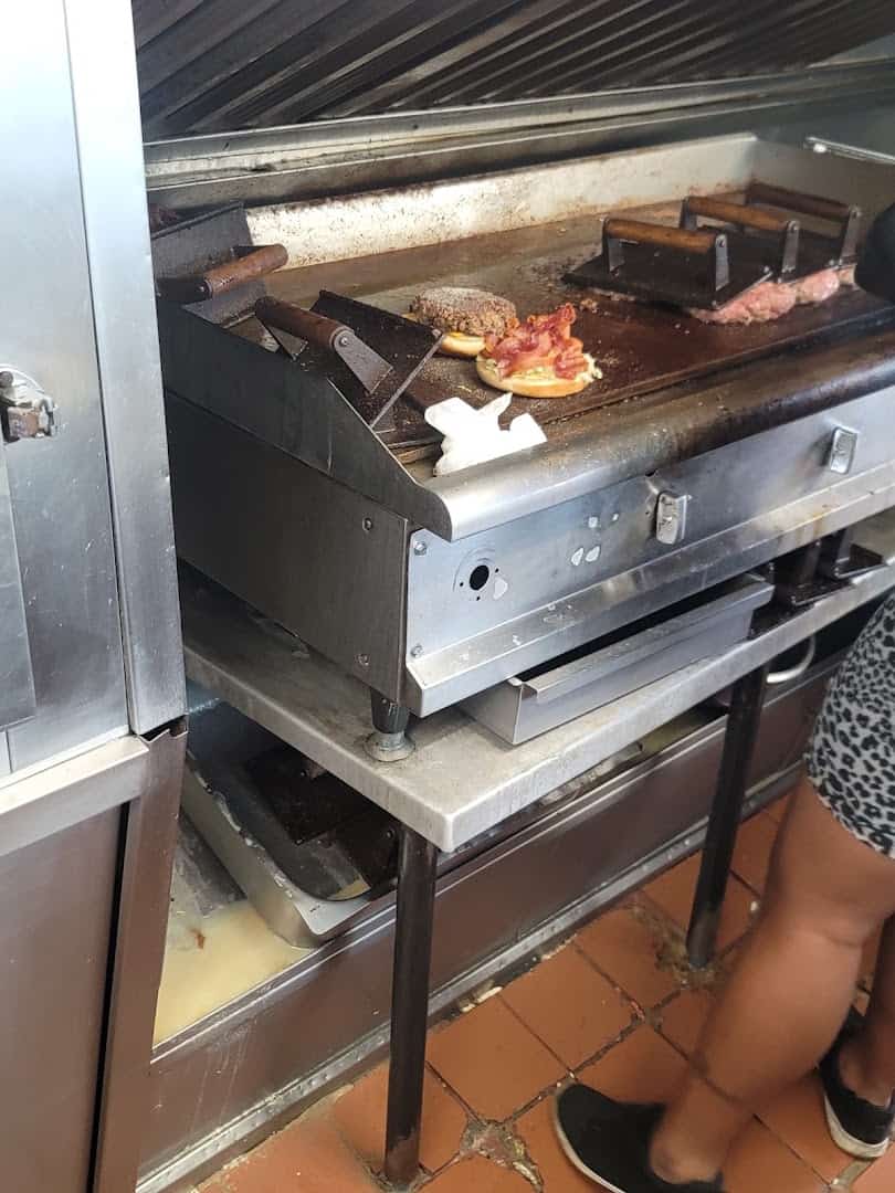Burger patties and bacon cooking under a press on the griddle at Wingfield's in Dallas